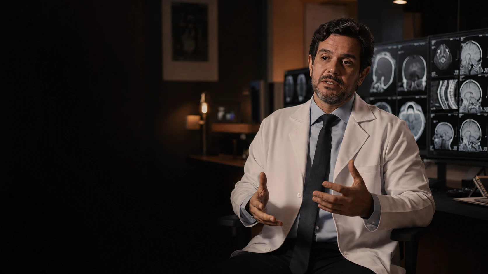 Radiologista em entrevista ao lado de monitores de imagem